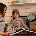 A mother and daughter enjoy reading a cookbook in a modern kitchen, sharing fun and learning together.