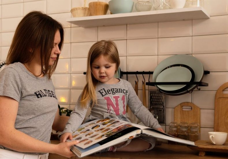 A mother and daughter enjoy reading a cookbook in a modern kitchen, sharing fun and learning together.
