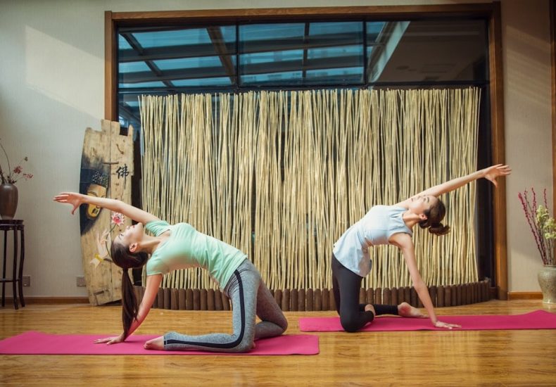 woman in white tank top and blue leggings doing yoga on purple yoga mat
